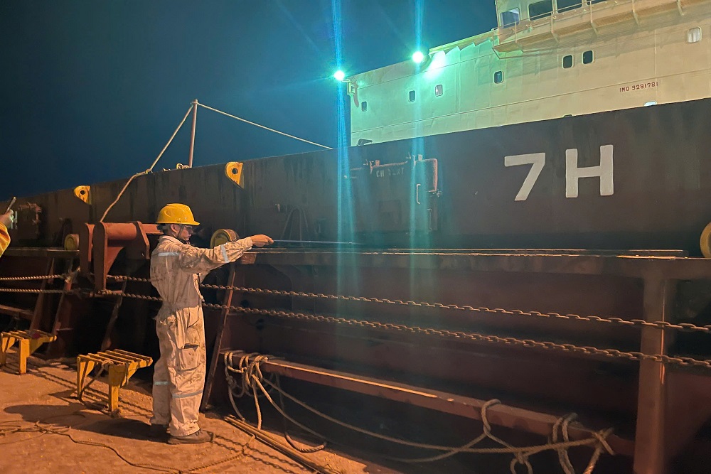 Technician performing ultrasonic tightness testing on a bulk carrier hatch cover at night